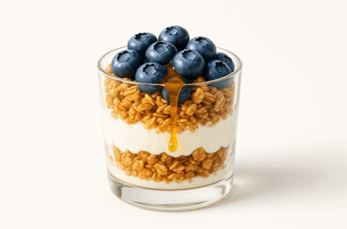 Glass cup layered with Greek yogurt, granola, blueberries, and honey drizzle.