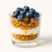 Glass cup layered with Greek yogurt, granola, blueberries, and honey drizzle.