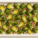 Roasted Brussels sprouts with crispy pancetta on a white baking tray.