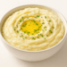 Bowl of creamy mashed potatoes topped with melted butter and chopped parsley.