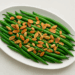 Green beans topped with toasted almonds and lemon zest on a white platter.