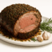 Herb-crusted prime rib roast on a white platter with rosemary and garlic cloves.