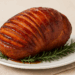 Glazed spiral ham with caramelized brown sugar and honey, garnished with rosemary on a white platter.