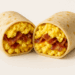 Cut-open breakfast burrito showing scrambled eggs, bacon, and cheese inside a tortilla.