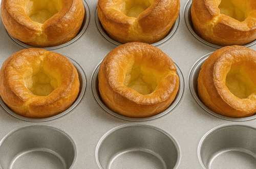 Golden Yorkshire puddings in a silver metal muffin tin on a white background.