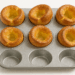 Golden Yorkshire puddings in a silver metal muffin tin on a white background.