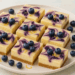 Lemon blueberry cheesecake bars with blueberry swirls and graham cracker crust on a white plate.